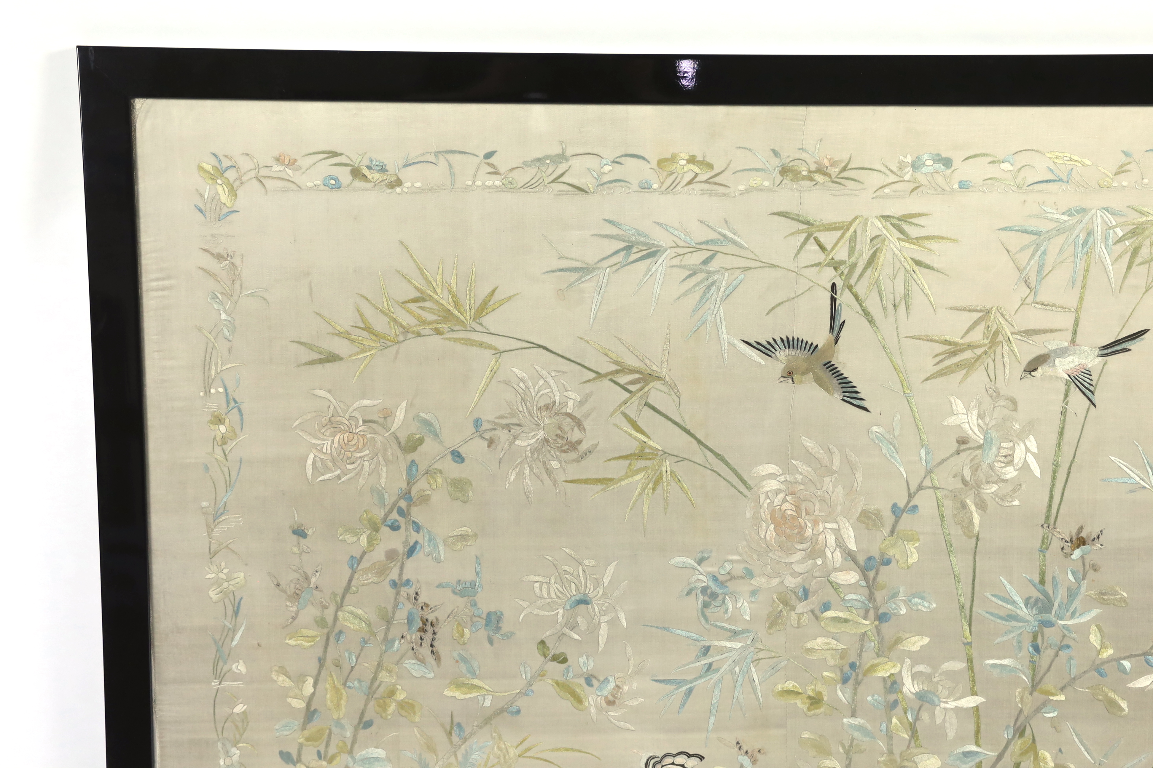 A framed early 20th century Chinese silk embroidered shawl, embroidered with chickens, ducks, flying birds and insects amongst bamboo and flowering plants, 126cm wide x 10.5cm high